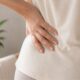 Woman's hand on lower back representing the connection between pelvic floor dysfunction and lower back pain in women over 40