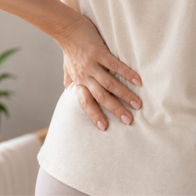 Woman's hand on lower back representing the connection between pelvic floor dysfunction and lower back pain in women over 40