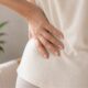 Woman's hand on lower back representing the connection between pelvic floor dysfunction and lower back pain in women over 40