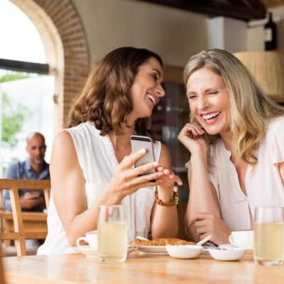 Leaking when you laugh — woman laughing with a friend at a café — a common but rarely discussed pelvic floor issue